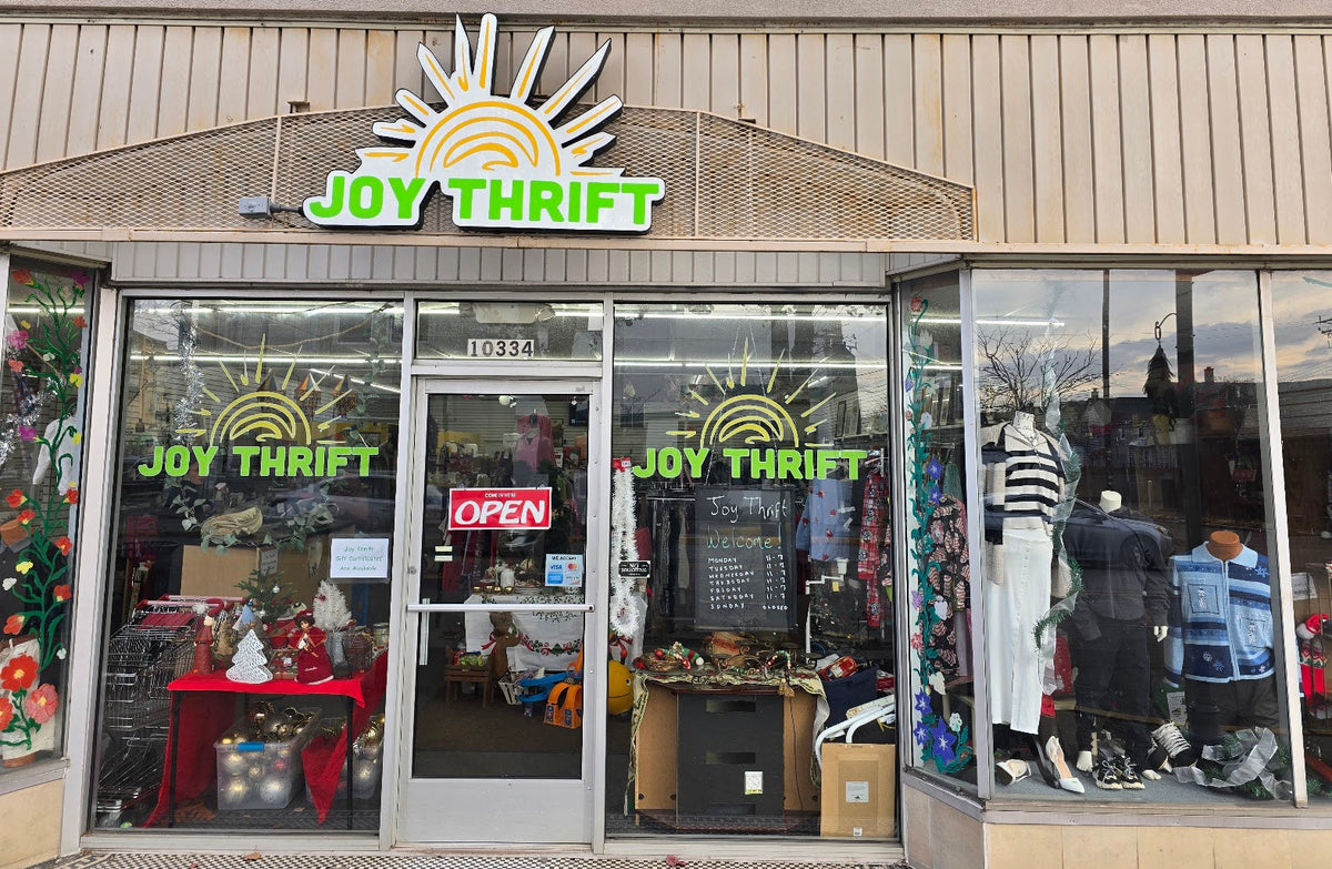 Front of a thrift store named 'Joy Thrift' with glass windows and visible merchandise.
