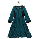 A women's long-sleeve dress with a teal and black horizontal stripe pattern, featuring solid black contrast panels on the shoulders, front placket, cuffs, and pockets, hanging on a white hanger against a wrinkled light gray fabric backdrop.