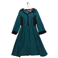 A women's long-sleeve dress with a teal and black horizontal stripe pattern, featuring solid black contrast panels on the shoulders, front placket, cuffs, and pockets, hanging on a white hanger against a wrinkled light gray fabric backdrop.