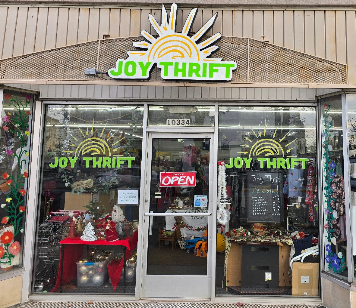 Front of a thrift store named 'Joy Thrift' with glass windows and visible merchandise.