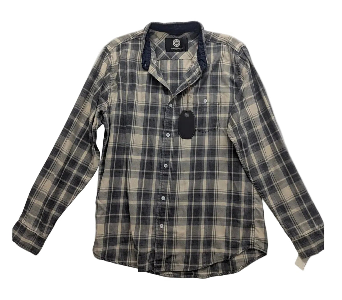 A long-sleeve plaid button-up shirt laid flat on a wrinkled light gray fabric background. The shirt features a beige and dark gray/black plaid pattern with a dark navy collar lining and a black hangtag attached.
